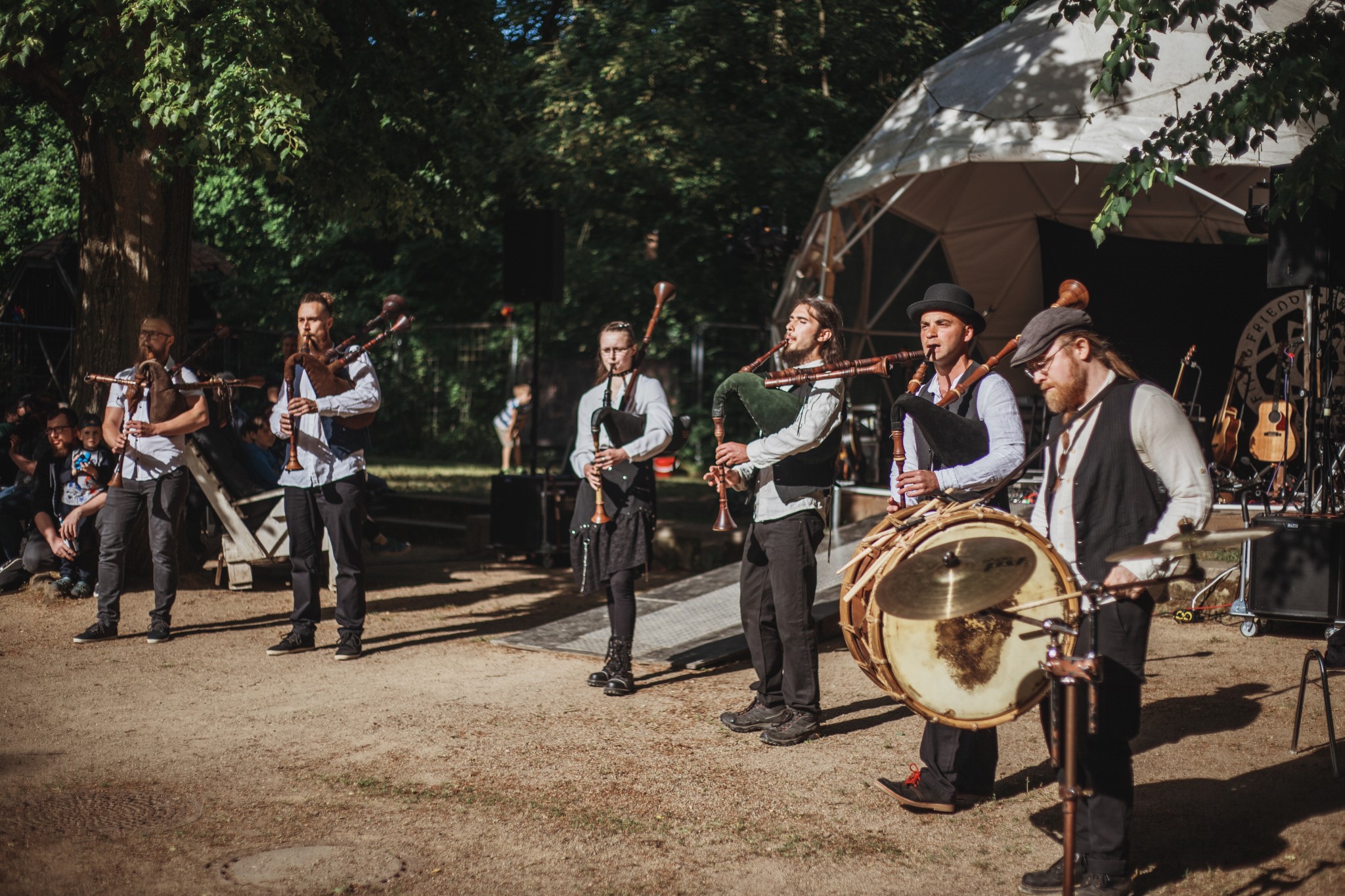 6 Musiker davon eine Dudelsackspielerin, 4 Dudelsackspieler und ein Trommler die in der Sonne Stehen und ein Konzert spielen.